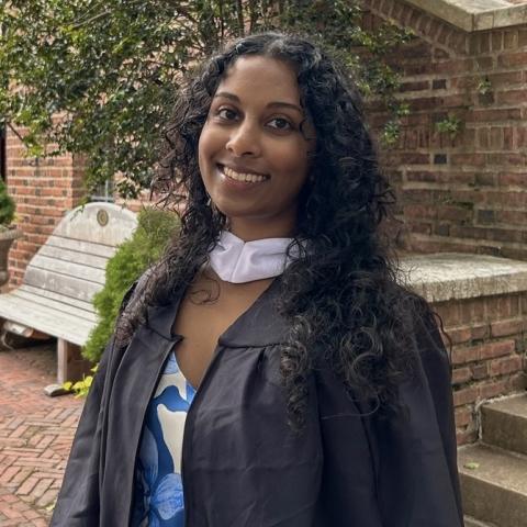 Maya standing in a courtyard in a graduation gown